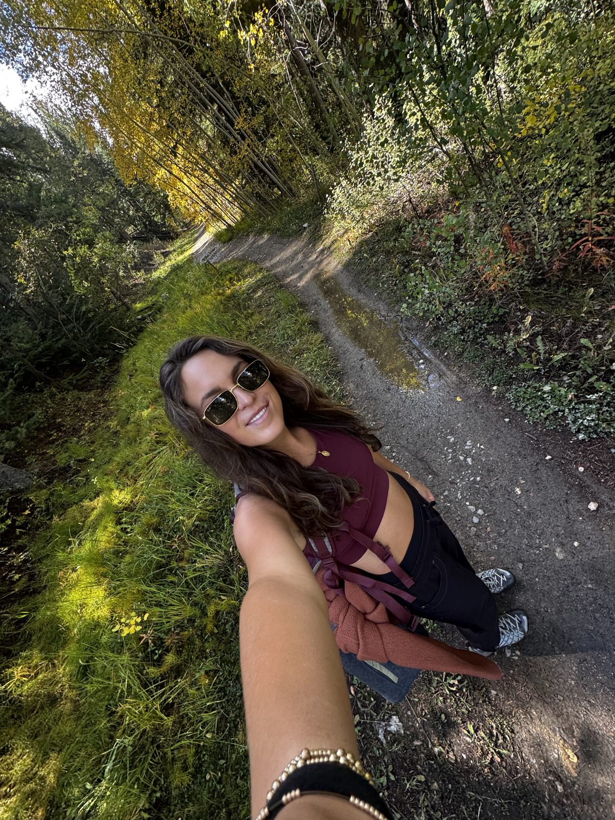 Olivia taking a selfie on a hiking trail through a sunlit forest