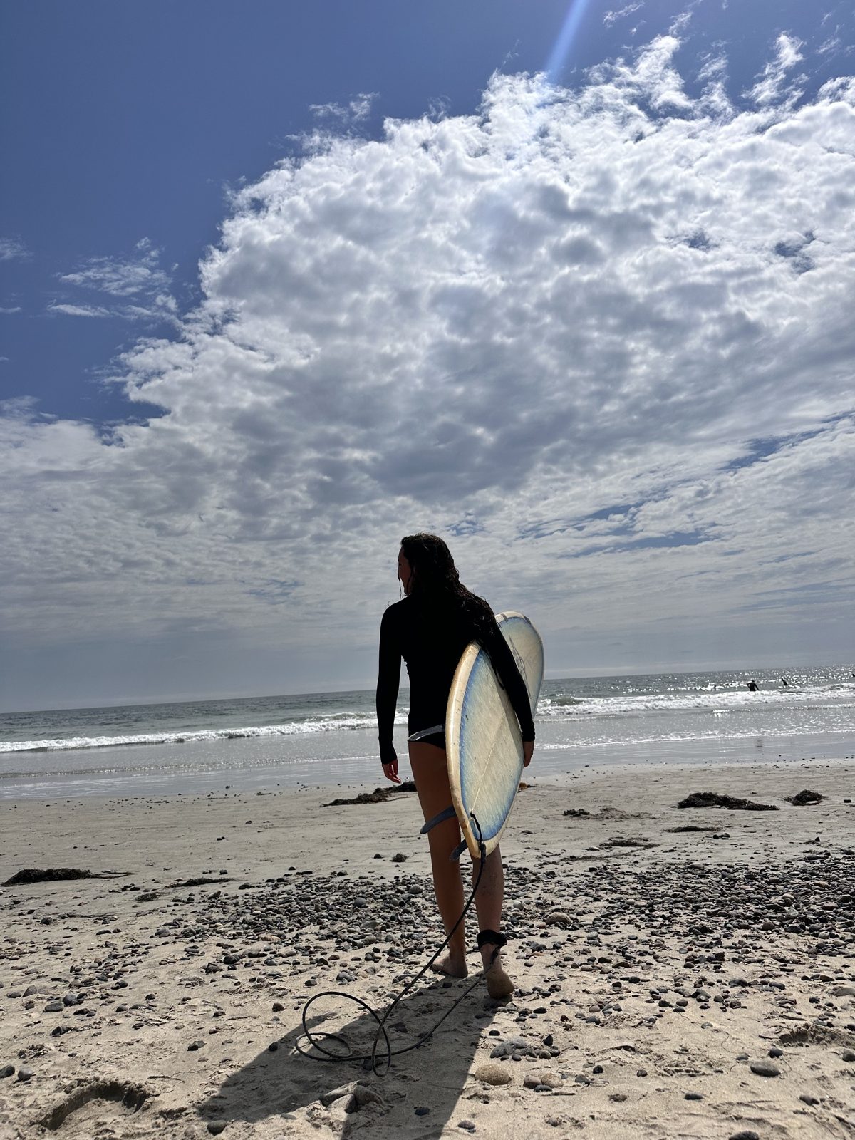 Olivia carrying a surfboard along a sandy beach toward the ocean